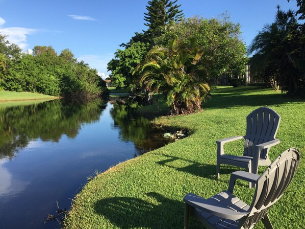 A serene lakeside setting with a chair and a table, surrounded by lush greenery and trees. - Great family home with a new sparkling pool,lovely lake view, 5 Minutes to beach (Naples)