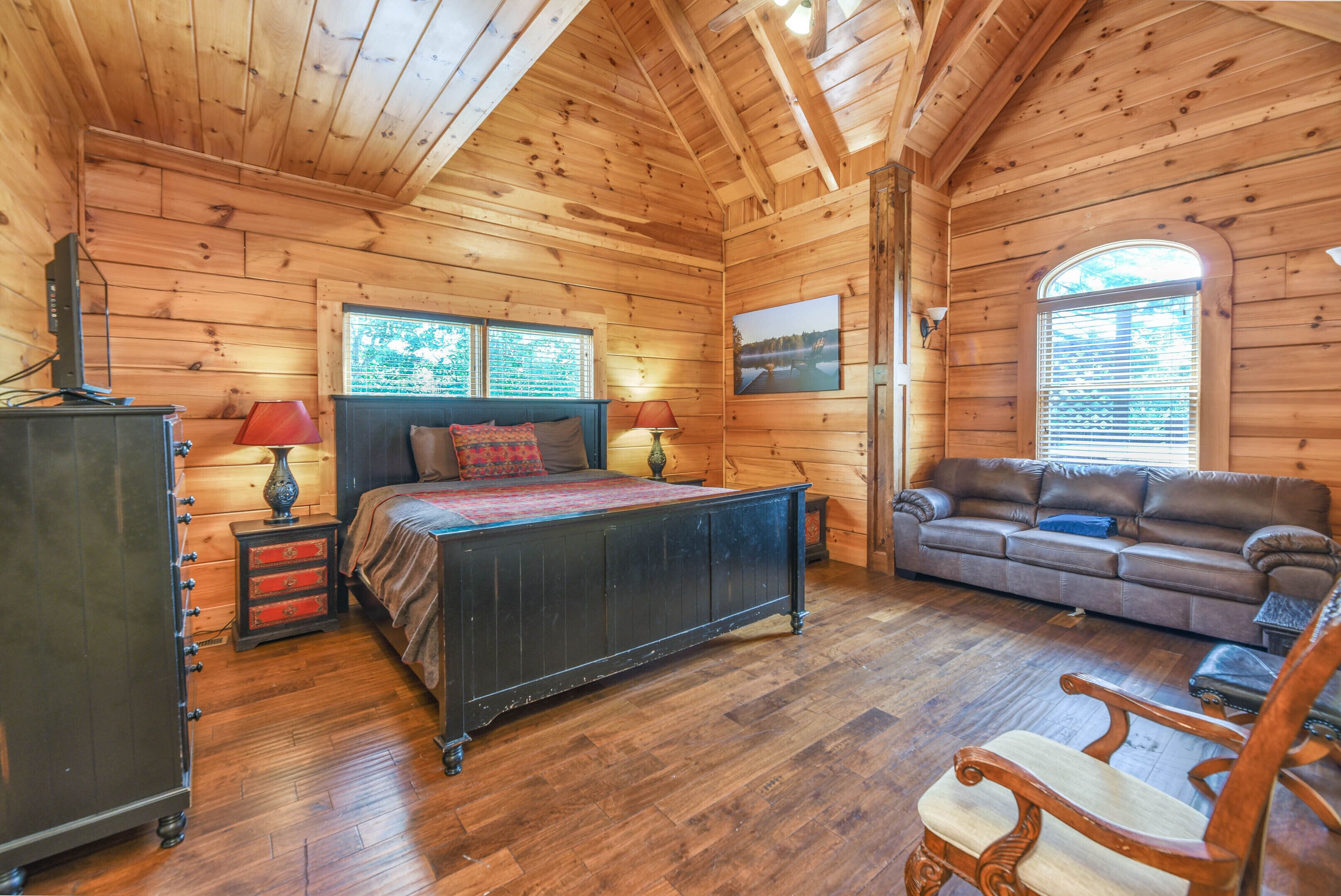 A log cabin bedroom with a bed, dresser, and a sofa.