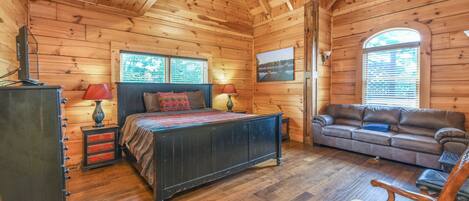 A log cabin bedroom with a bed, dresser, and a sofa.