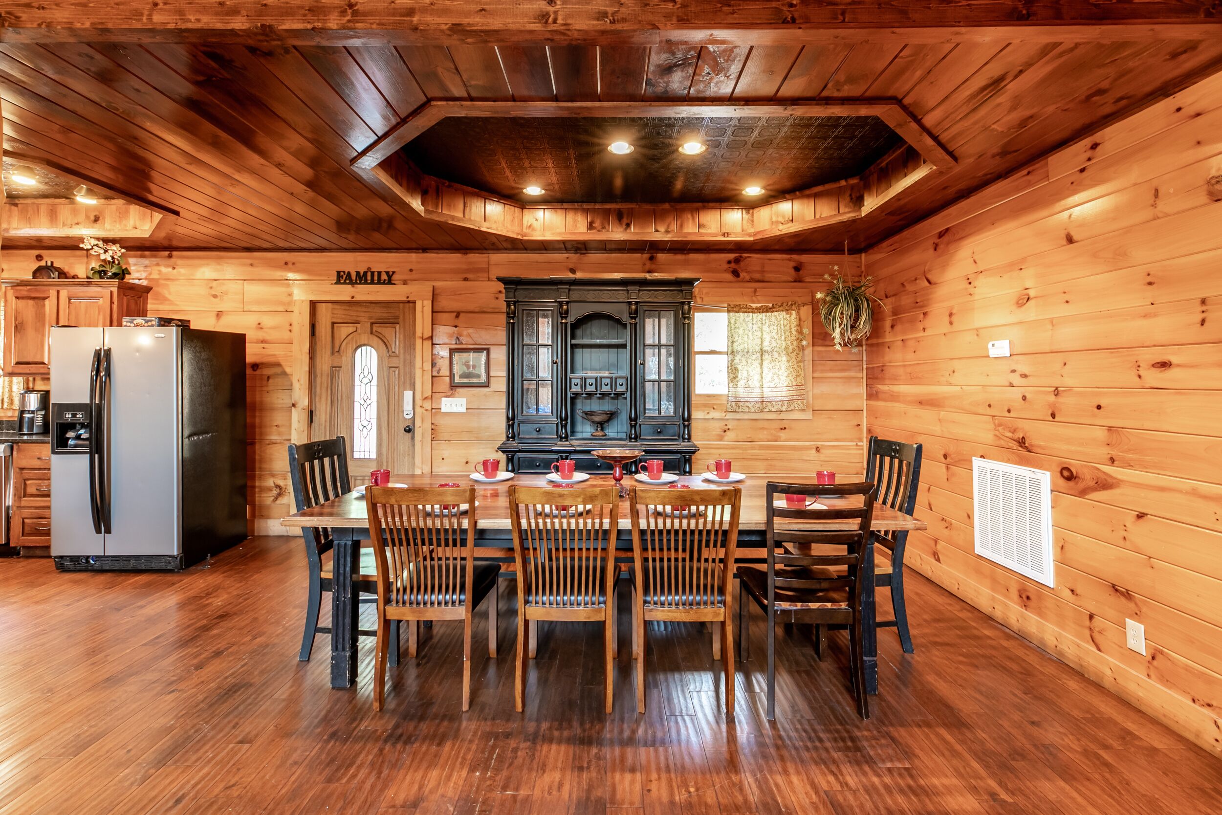 A wooden cabin interior with a dining table, chairs, a refrigerator, and a kitchen area.