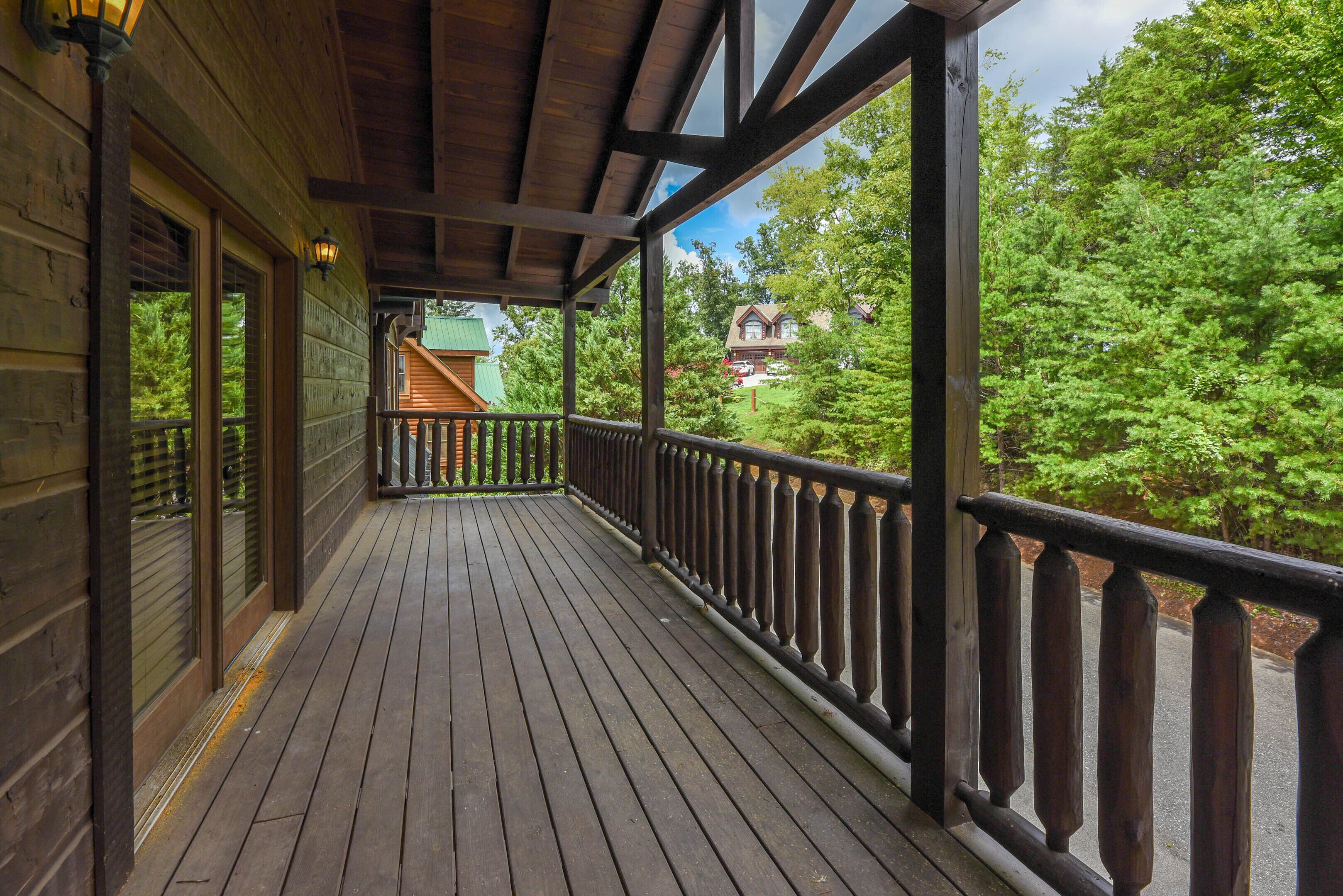 A wooden deck with a railing, a covered porch, and a view of a house and trees.