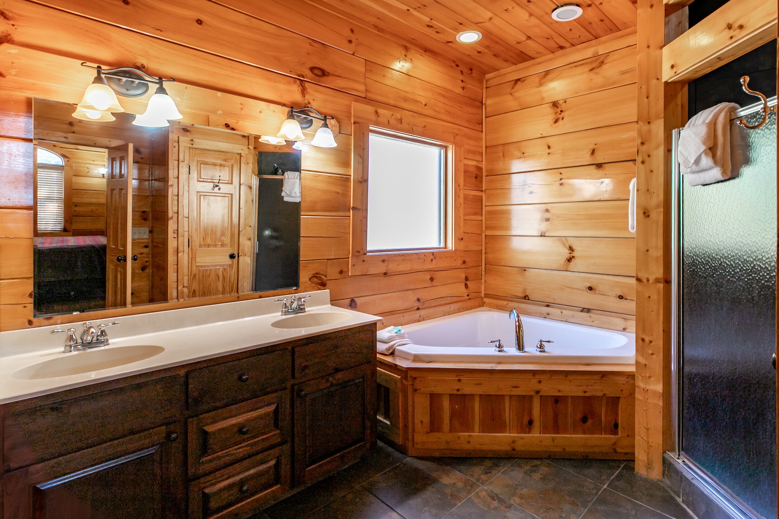 A wooden cabin bathroom with two sinks, a large bathtub, and a mirror.