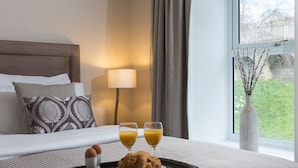 A neatly made bed with a tray of breakfast including eggs, a croissant, and two glasses of orange juice. - 12 Pear Tree House - sleeps 4 guests  in 2 bedrooms (York)