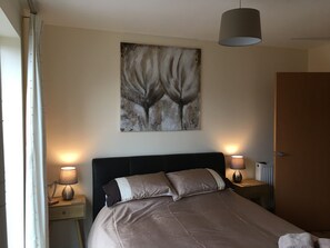 Une chambre à coucher avec un lit, deux lampes de chevet, un tableau accroché au mur et une porte.