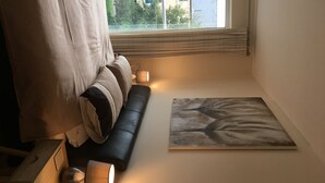 A small, cozy room with a black sofa, a painting on the wall, and a window with blinds. - Penthouse Apartment on the River - Little Paxton (Saint Neots)