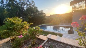 A swimming pool surrounded by lush greenery and flowering plants, with a view of the sunset in the background. - Studio Anemone: self-catering cottage in Sarlat with private heated pool (Sarlat-la-Canéda)