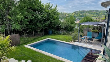 Ein rechteckiger Pool mit Holzdeck und einer Pergola mit Sonnenschirmen.