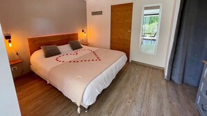 A bedroom with a wooden headboard, a bed with rose petals arranged in a heart shape, bedside lamps, and a view of greenery through a window. - Studio Anemone: self-catering cottage in Sarlat with private heated pool (Sarlat-la-Canéda)
