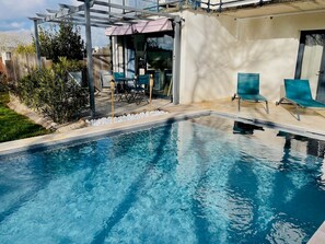 Une piscine dotée d’une pergola et de chaises, entourée d’un jardin et d’un bâtiment.