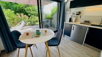 Une cuisine moderne avec un coin repas, une vue sur la verdure et un petit espace extérieur aménagé pour s’asseoir.