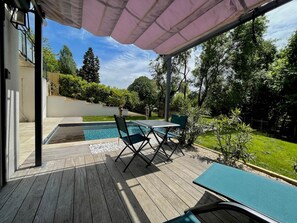 Un espace extérieur abrité comprenant une piscine, une terrasse en bois et des sièges.