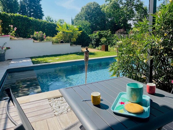 Un espace aménagé au bord de la piscine, avec une table, un plateau pour les boissons et une piscine agrémentée d’un élément décoratif aquatique.
