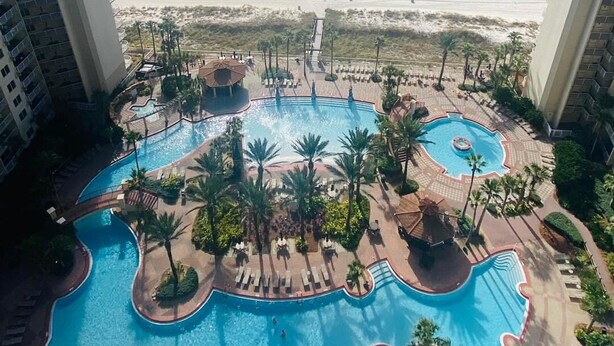 Un resort con diverse piscine, palme e vista sulla spiaggia.