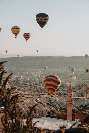 Vista de un pueblo con varios globos aerostáticos en el cielo y un minarete destacado al frente.