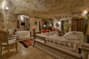Un dormitorio con una cama grande, una zona de estar con una silla, una bañera y un espejo.