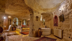 Habitació amb paret de pedra, banyera, cadira de fusta i llit amb catifes vermelles.