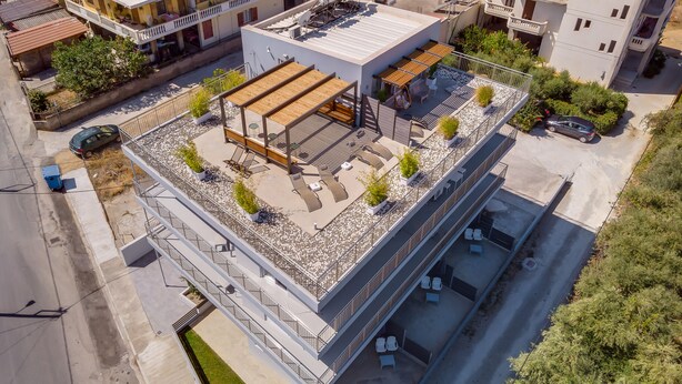 Vista aérea de un edificio moderno con zona de patio en la azotea, varios balcones y un estacionamiento.