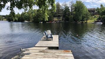 Une jetée en bois s’étendant sur un lac paisible, entourée d’arbres et d’un bâtiment situé au loin.