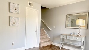 A room with a wooden floor, a white door, a staircase, a vanity with a mirror, and two framed pictures on the wall. - Spacious Townhouse. 3B & 1. 5 baths. 10 Min to Airport. Free parking. (North Charleston)