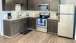 A modern kitchen with dark wood cabinets, a stainless steel microwave, a refrigerator, a stove, and a tiled backsplash. - Spacious Townhouse. 3B & 1. 5 baths. 10 Min to Airport. Free parking. (North Charleston)