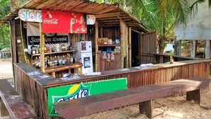 Een strandbar met een Coca-Cola bord, een koelkast vol drankjes en een bank.