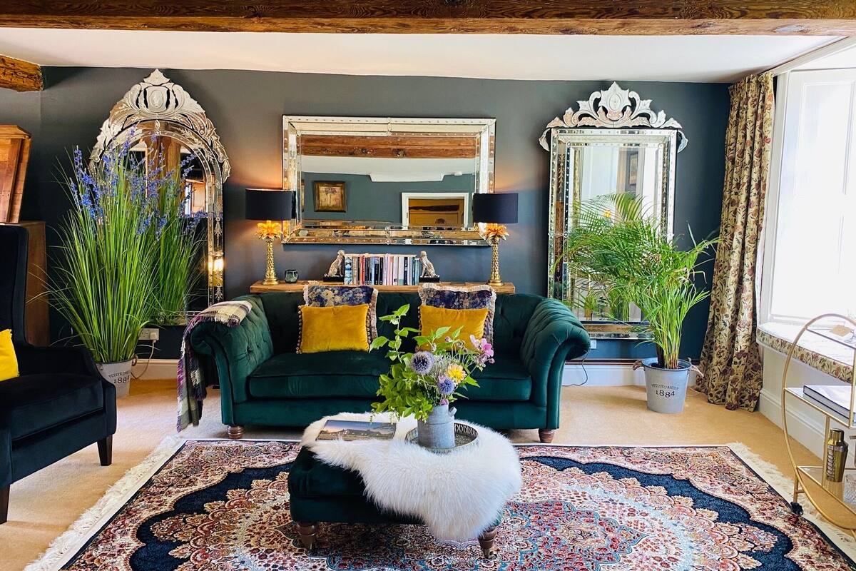 A cozy living room with a dark green sofa, a white furry ottoman, and a large mirror.