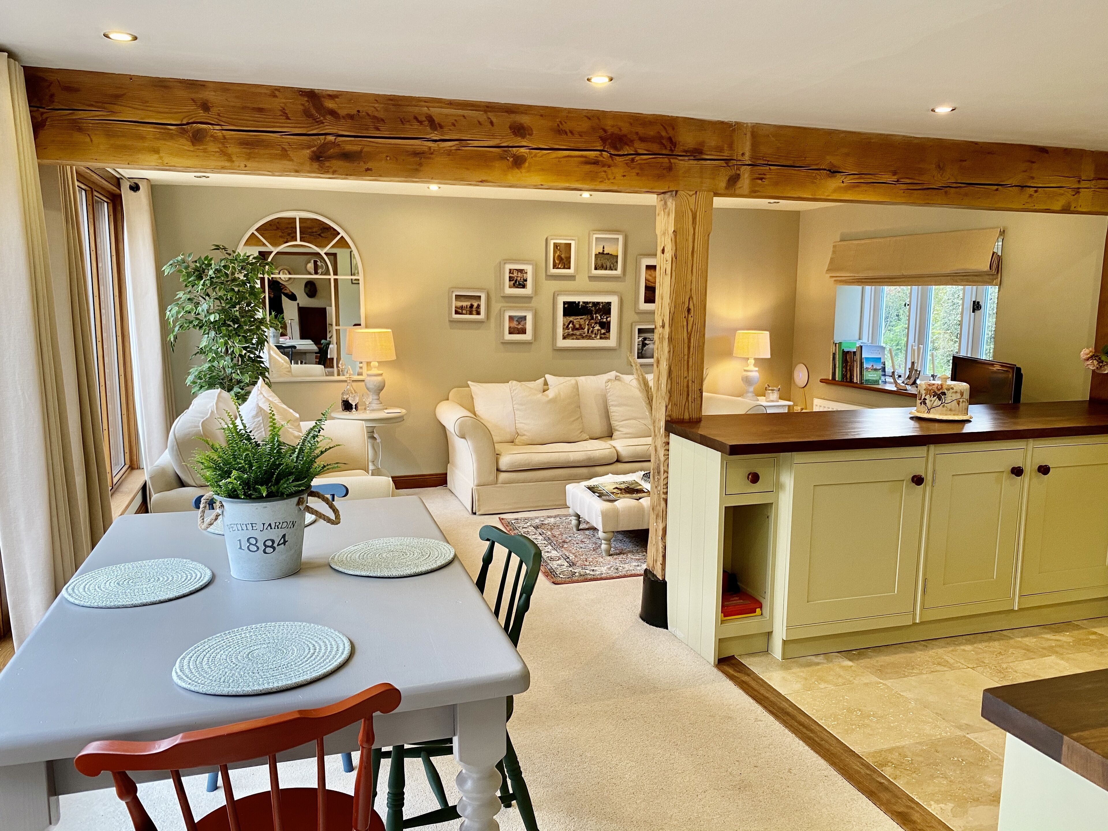 A cozy living room with a dining area, wooden beams, and a kitchen with a window.