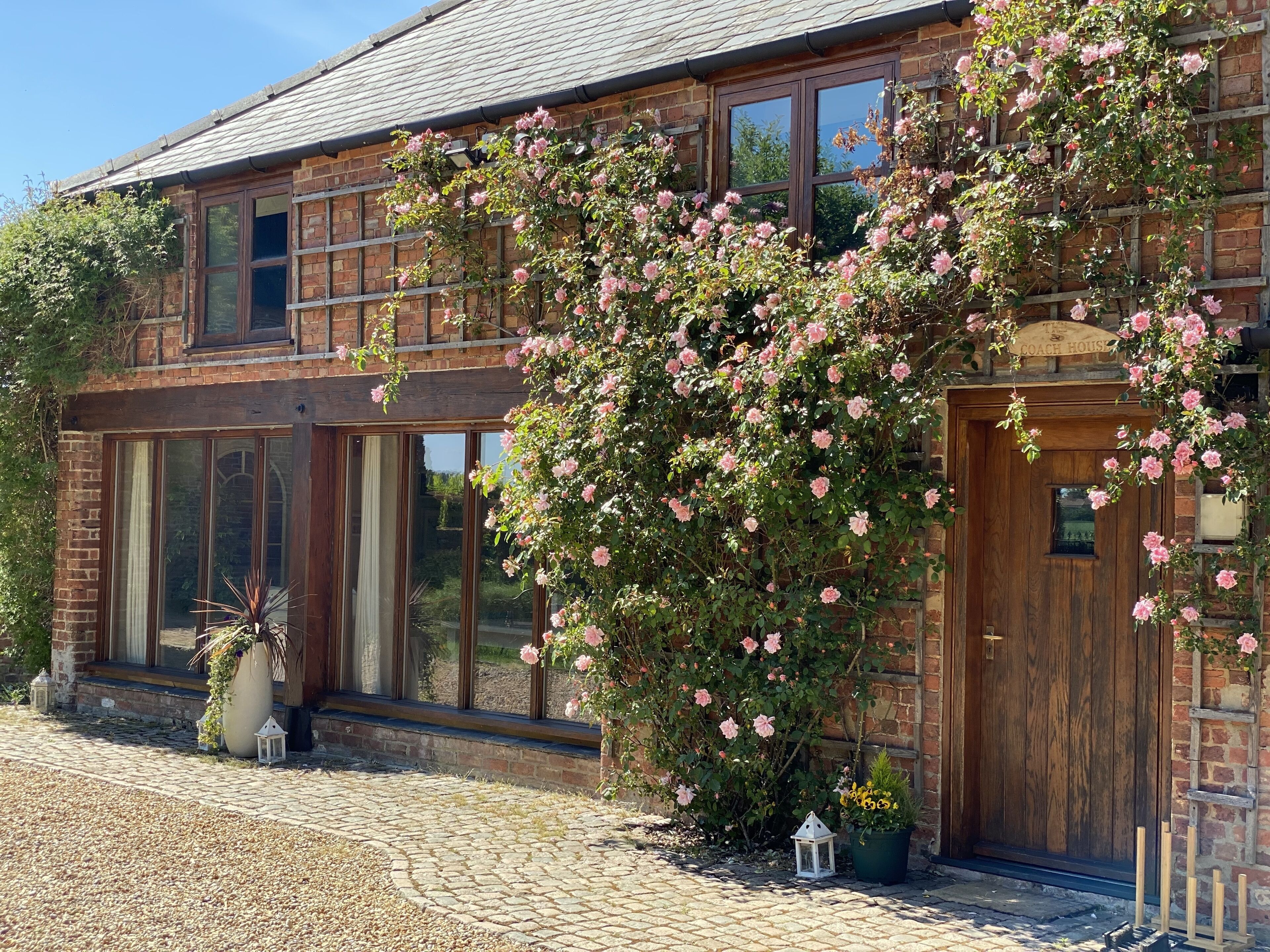 A brick building with large windows and a wooden door, surrounded by blooming pink roses.