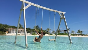 A wooden swing set over clear turquoise water with a beach and palm trees in the background. - Luxury Catamaran Sailing Trips in the Exumas & Staniel Cay area (Staniel Cay)