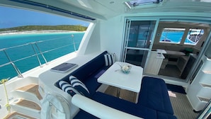 A boat deck with a seating area, a table, and a view of the ocean. - Luxury Catamaran Sailing Trips in the Exumas & Staniel Cay area (Staniel Cay)