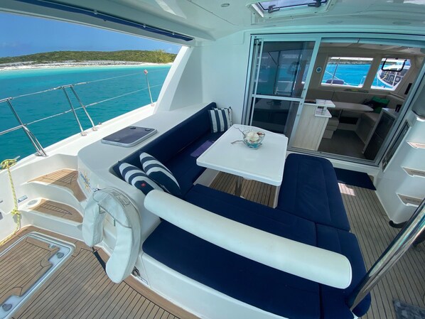A boat deck with a seating area, a table, and a view of the ocean.