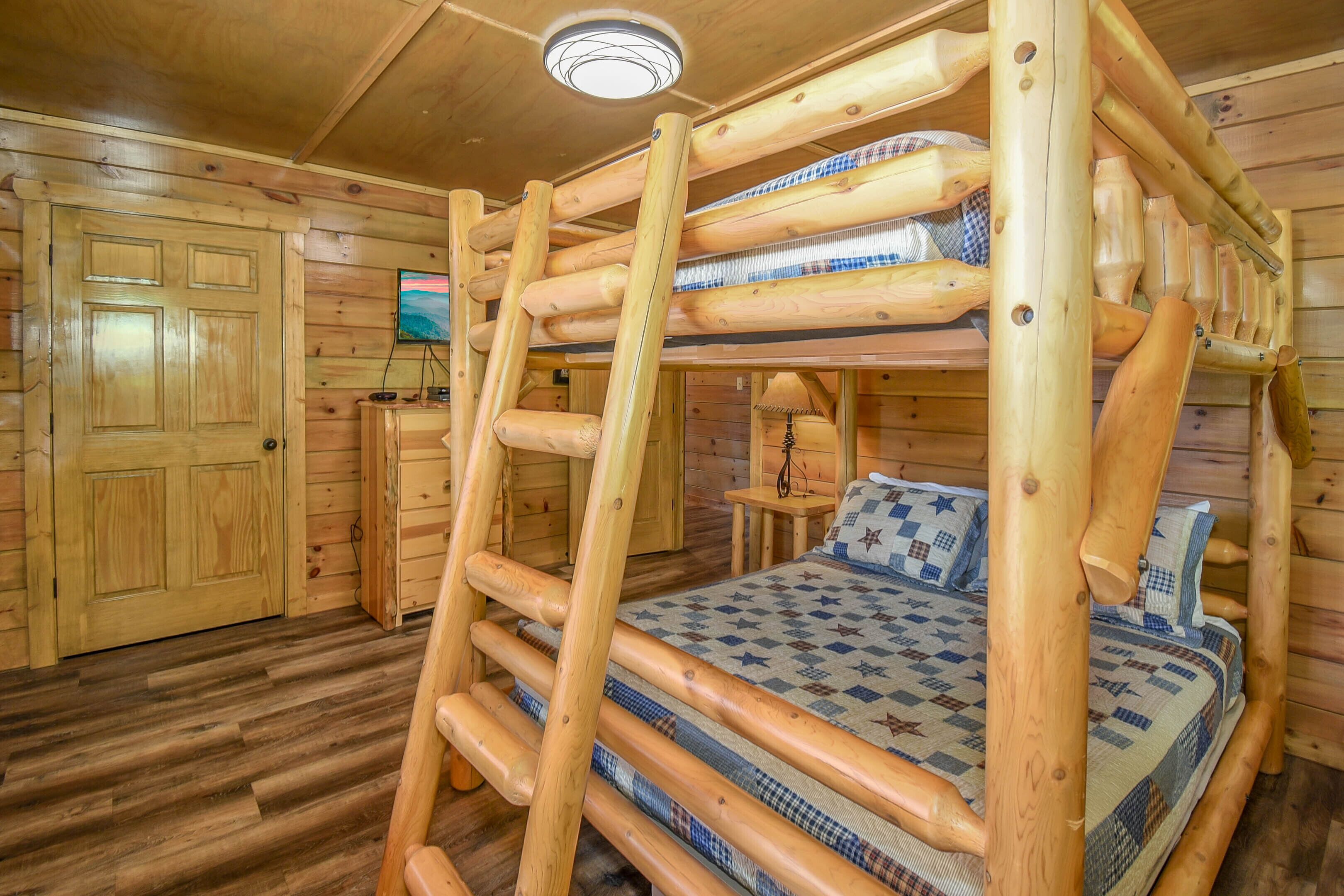 A wooden cabin room with a bunk bed, wooden walls, a wooden door, a small table, and a television on the wall.