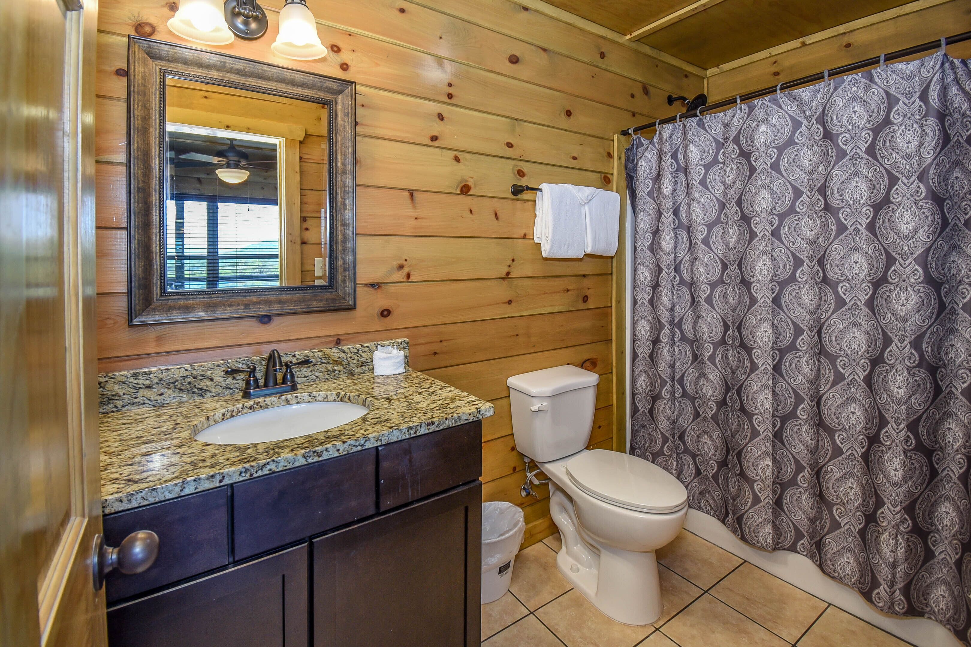 A wooden-paneled bathroom with a granite countertop sink, a toilet, and a patterned shower curtain.