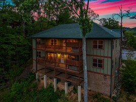 A two-story cabin with a balcony, surrounded by trees and a lake.
