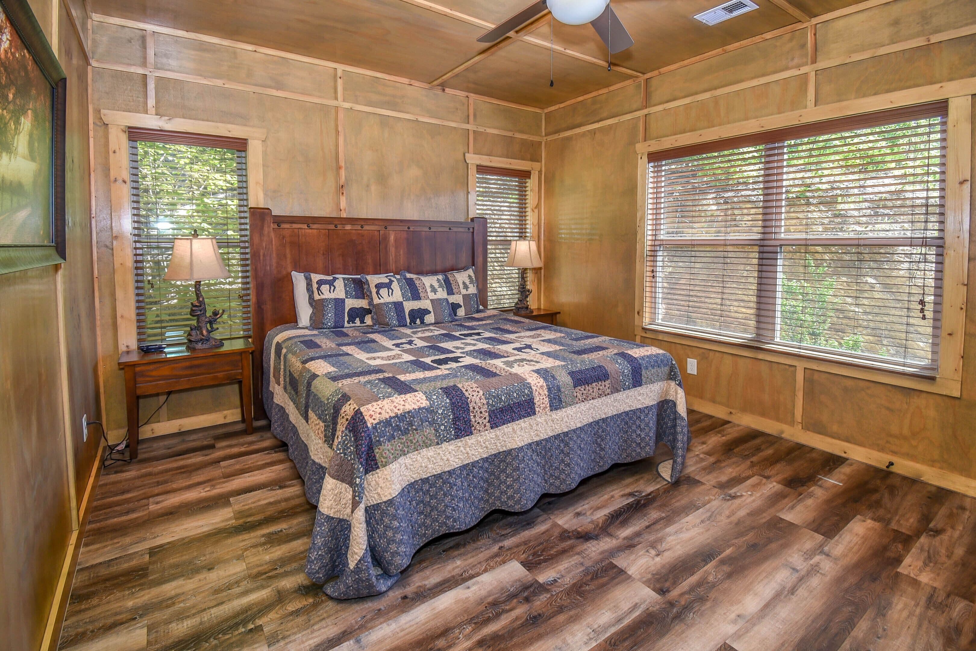 A wooden-paneled bedroom with a large bed, two bedside tables with lamps, and windows with blinds.
