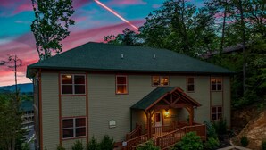 A two-story lodge with a porch and a covered entrance, surrounded by trees and a view of the mountains. - SmokyStays 10 Bedroom Cabin (Pigeon Forge)