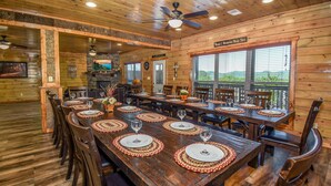 A wooden dining area with a long table set for a meal, surrounded by chairs. - SmokyStays 10 Bedroom Cabin (Pigeon Forge)