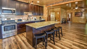 A kitchen with dark wooden cabinets, stainless steel appliances, a granite countertop, and a central island with bar stools. - SmokyStays 10 Bedroom Cabin (Pigeon Forge)