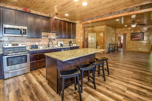 A kitchen with dark wooden cabinets, stainless steel appliances, a granite countertop, and a central island with bar stools.