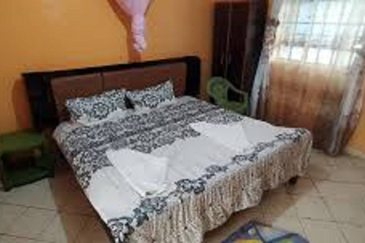 A bedroom with a bed, a nightstand, a chair, and a window with curtains.