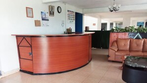 A reception area with a curved wooden desk, a brown leather sofa, and a black chair. - Dayton Hotel (Nakuru)