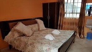 A bed with a floral bedspread, a wooden headboard, and a window with curtains. - Dayton Hotel (Nakuru)