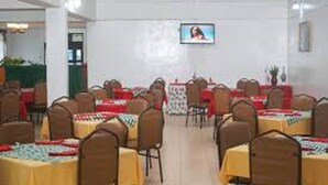 A dining area with tables set for multiple people, chairs arranged around each table, and a television mounted on the wall. - Dayton Hotel (Nakuru)