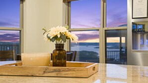 A kitchen counter with a wooden tray holding a candle and a vase of flowers, with a view of the sunset through large windows. - Lake View Escape - Sleeps 22, Game Room, Indoor Pool (Branson)