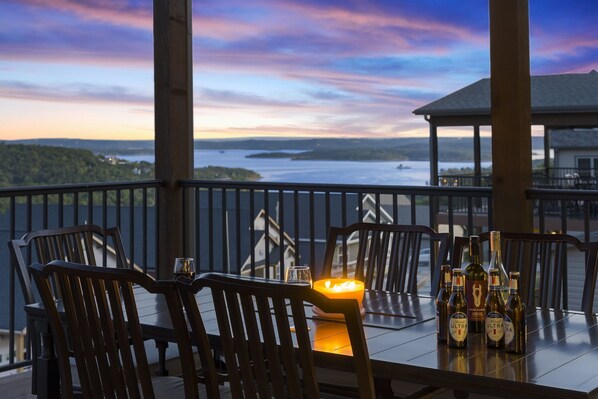 A table with chairs and bottles of beer, a candle, and a view of a lake at sunset.