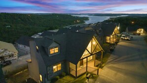 A residential area with houses featuring steep gabled roofs and large windows, surrounded by a body of water and greenery. - Lake View Escape - Sleeps 22, Game Room, Indoor Pool (Branson)