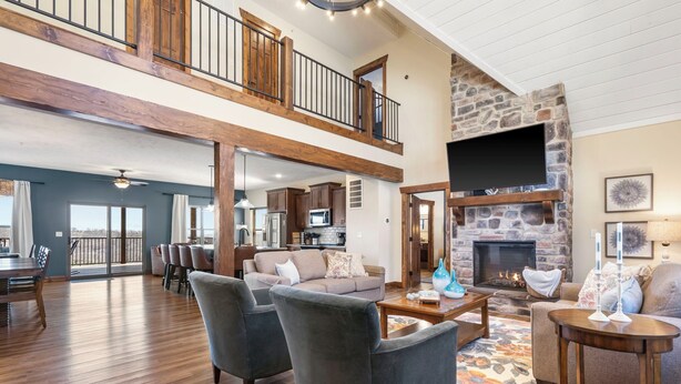 A spacious living area with a high ceiling, wooden beams, a stone fireplace, and a balcony. - Lake View Escape - Sleeps 22, Game Room, Indoor Pool (Branson)
