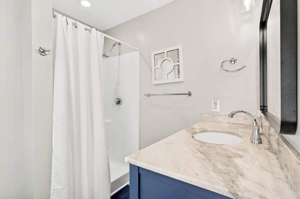 A bathroom with a shower, a sink, a mirror, and a towel rack.