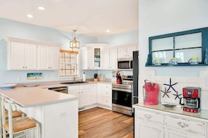 A kitchen with white cabinets, a central island, a microwave, a stove, and a coffee maker. - Fishful Thinking by Brunswick Vacation Rentals: Canalfront w/ Dock, Kayak & More (Ocean Isle Beach)