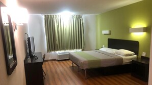 A hotel room with a bed, bedside table, a desk with a computer, a mirror, and a window with curtains. - Shadeland Inn Indianapolis (Indianapolis)